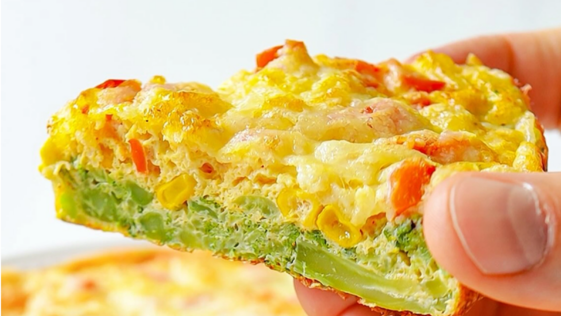 Fatia de torta de brócolis saudável sendo segurada pela mão, mostrando o recheio suculento com milho, pimentão e queijo derretido